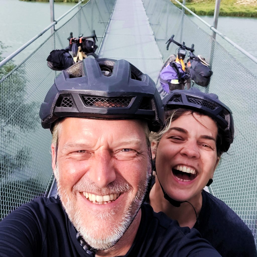 Alexandra und Matthias haben Fahrradhelme und lachen in die Kamera. Im Hintergrund sieht man ihre Fahrräder.